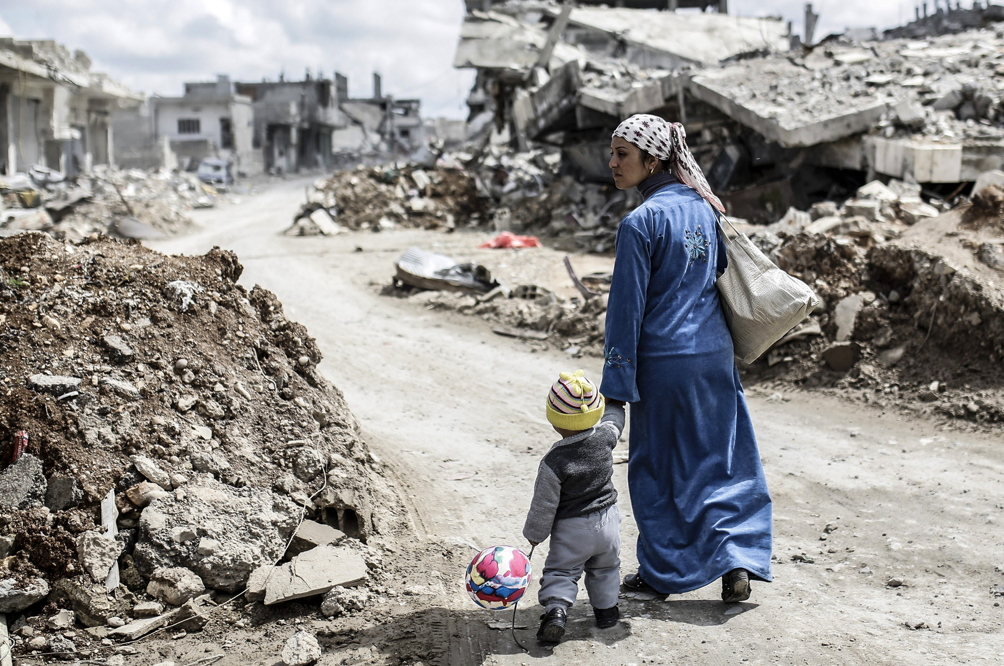 SYRIA-KURDS-CONFLICT A Kurdish Syrian woman walks with her child past the ruins of the town of Kobane, also known as Ain al-Arab, on March 25, 2015. Islamic State (IS) fighters were driven out of Kobane on January 26 by Kurdish and allied forces. AFP PHOTO/YASIN AKGUL (Photo credit should read YASIN AKGUL/AFP/Getty Images)